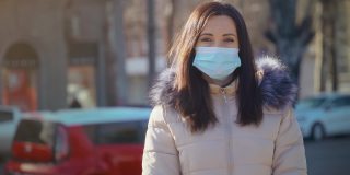 白天，一名留着黑色长发的女子站在城市街道上，戴着口罩，以抵御空气污染和冠状病毒