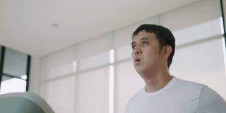 一个亚洲人在健身房跑步机上跑步的中景镜头。