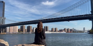 年轻美丽的女人坐在堤岸的石头上，在Dumbo，布鲁克林