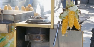 路边摊柜台上的新鲜玉米。街头小吃，小贩在城市的街道上向顾客出售排成一排的煮玉米。健康食品和产品的理念，行人路过