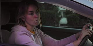 一个年轻的女人坐在右手边一辆车的方向盘后面，紧张地看着后视镜，等着警察来。警笛灯在闪烁。超速罚单