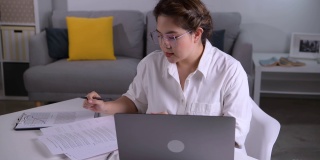 年轻的亚洲女性自由职业者在家里用电脑工作。有吸引力的女商人在线学习，使用笔记本电脑软件，网上冲浪信息或在网上商店购物