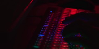在黑暗中工作的手。黑客在晚上工作。计算机安全威胁。晚上工作。秘密的工作。键盘的颜色是红色的