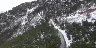 在冬天，汽车在雪山中行驶。在被绿色森林包围的雪山上飞行。山间的山路