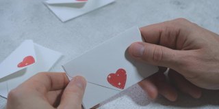 男人的手打开一个白色的信封，里面写着一颗心，抽出一张卡片，上面写着“我爱你”