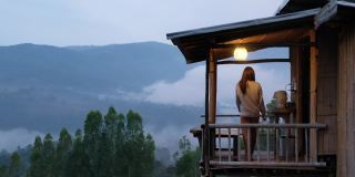 一个女人在木制房子的阳台上喝饮料，在雾天可以看到美丽的山景