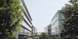城市办公大楼的混凝土通道，左侧有一扇网门，右侧有绿树和灌木