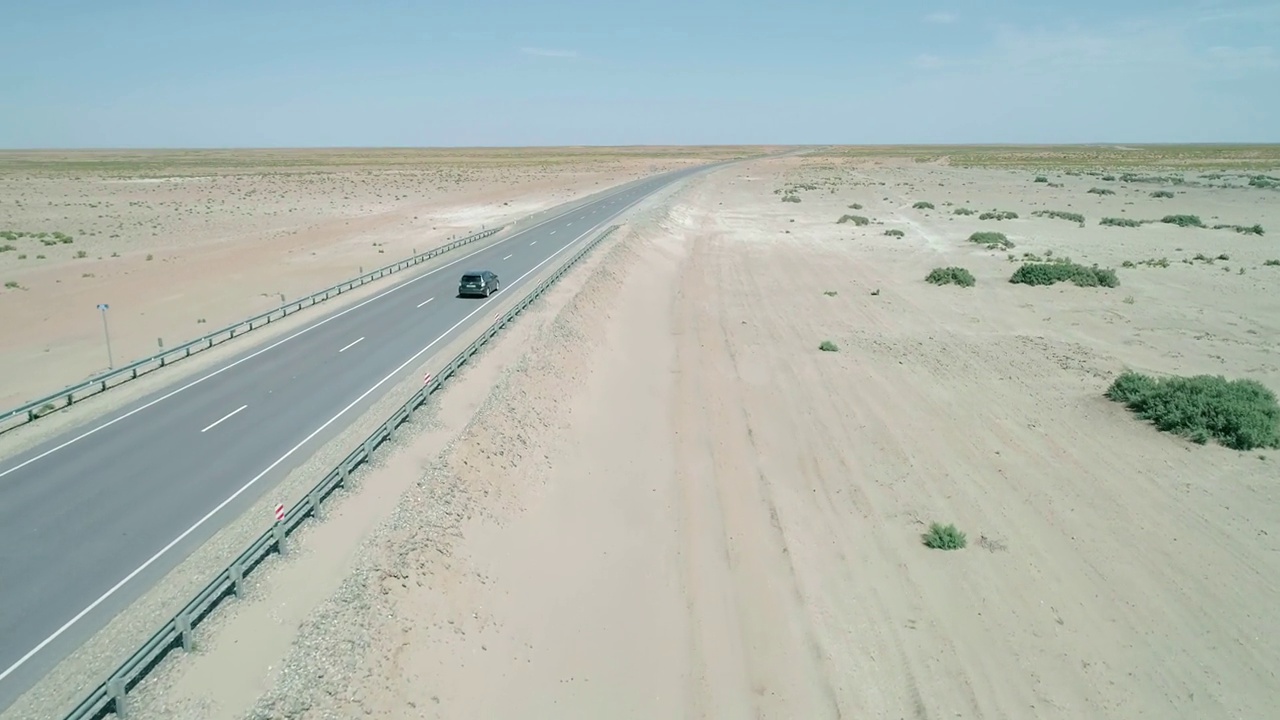 空中全景图，一辆汽车行驶在高速公路与小绿草灌木丛之间的沙子。