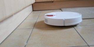 白色智能吸尘器清扫家里厨房的瓷砖地板。现代科技使生活更容易。特殊视频接收荷兰角