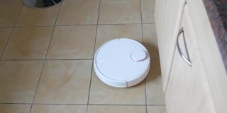 白色智能吸尘器清扫家里厨房的瓷砖地板。现代科技使生活更容易