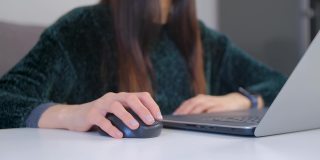 自由职业女性用无线电脑鼠标点击4k特写视频。企业家用笔记本电脑进行远程在线工作。封锁期间，女商人在家里用笔记本电脑工作