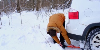 男子用铲车铲在雪地里挖出一辆熄火的汽车。冬天一场大雪过后，交通被困在了雪堆里，坐到了底部。急救，拖车，冬季轮胎钉和四季。慢动作