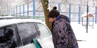 一名男子在雪后从车上刷雪。夹克里的一只手，白色的身体上放着一把汽车扫把。冬天的天气条件。慢动作