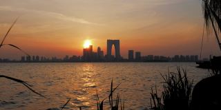 中国苏州- 2019年3月30日:日落时的天际线全景，城市摩天大楼在湖面上倒影