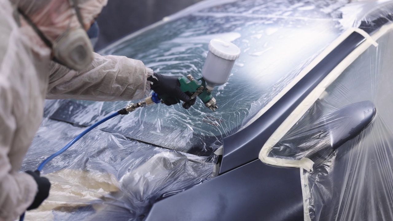 师傅在汽车维修中油漆汽车零件。他穿着防护服，手里拿着喷涂机。现代汽车绘画