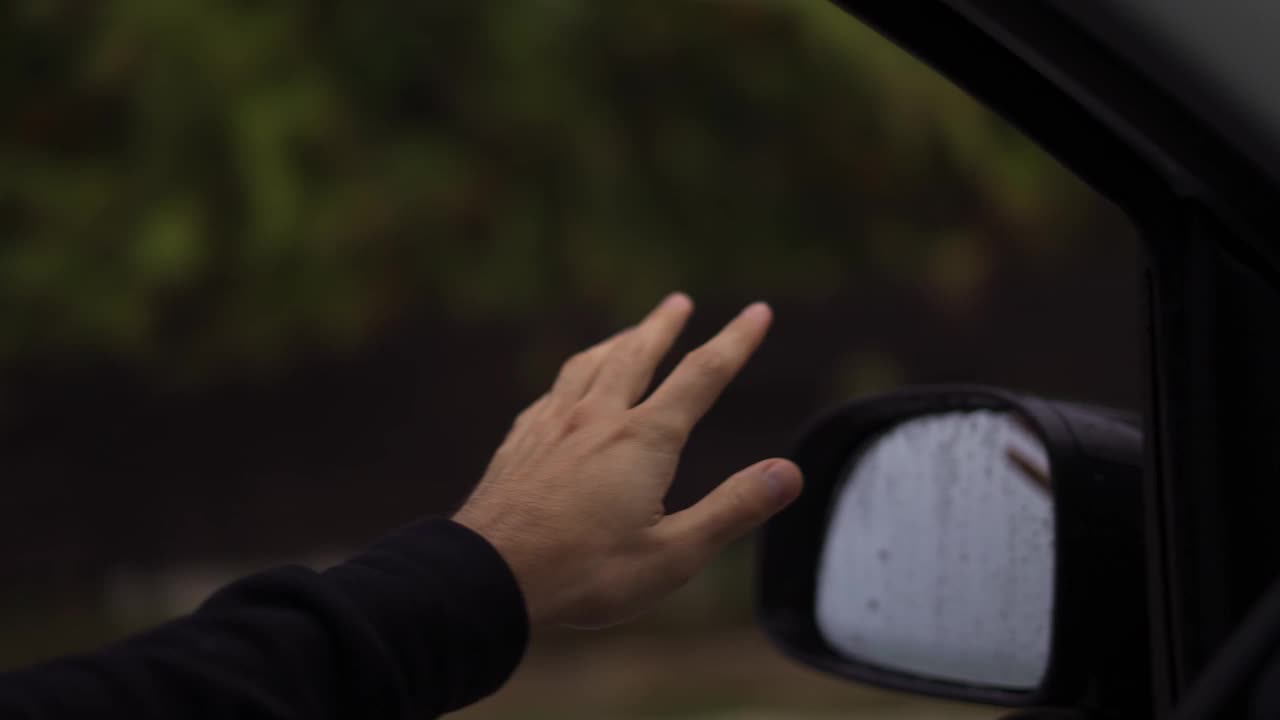 一个男人的手正在捕捉雨在一个雨天开车，慢动作