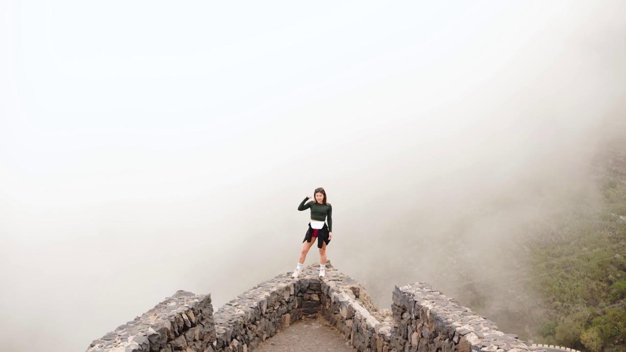 年轻的女旅行者站在悬崖边，观察山上的雾