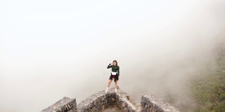 年轻的女旅行者站在悬崖边，观察山上的雾