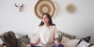 健康的生活方式。一个女人穿着休闲服在一个真实的房间里休息。在沙发上摆莲花姿势，冥想