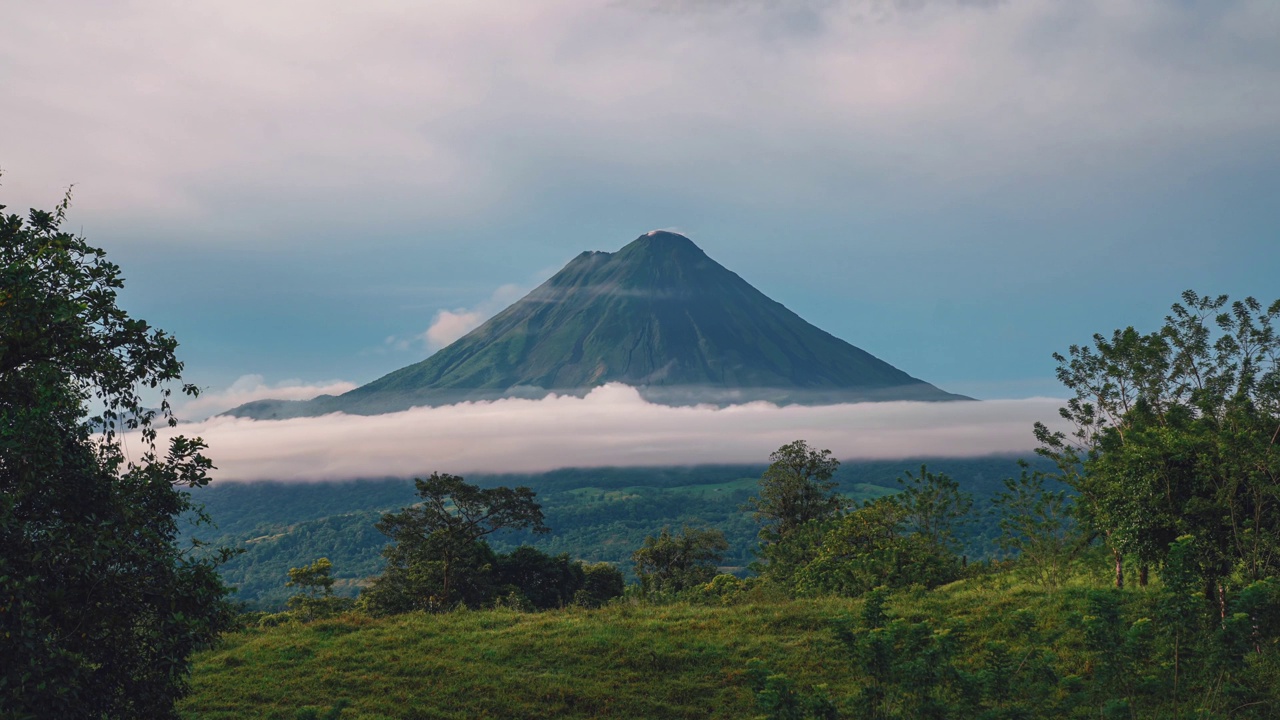 在哥斯达黎加拉福图纳，令人印象深刻的阿雷纳尔火山的延时摄影/无缝视频循环。小云朵在山顶上移动，火山烟雾从山顶升起。该地区以其温泉和郁郁葱葱的大自然而闻名。