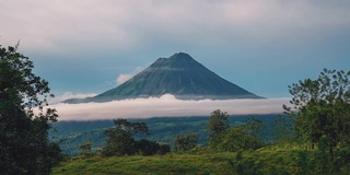 在哥斯达黎加拉福图纳，令人印象深刻的阿雷纳尔火山的延时摄影/无缝视频循环。小云朵在山顶上移动，火山烟雾从山顶升起。该地区以其温泉和郁郁葱葱的大自然而闻名。