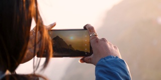 用智能手机拍摄女性手部特写，点击吉尔纳尔山的照片。摄影师创造多媒体内容的山在日出，妇女点击图片在徒步冒险