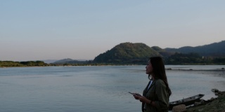 一位年轻的亚洲妇女站在湄公河边用手机