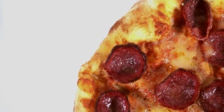 一个美味的意大利辣香肠披萨在桌子上旋转的微距镜头，孤立在白色背景上