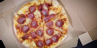 在桌子上方的纸箱上，人们的手拿着一片片的意大利辣香肠披萨