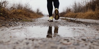 女人穿着运动运动鞋走，跑，跳水坑与水花和滴在秋天秋天