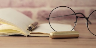 木桌上放着记事本、眼镜和一支钢笔