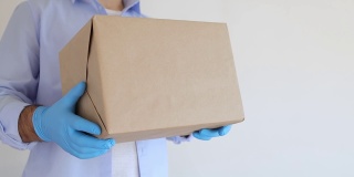 送货员拿着纸箱，戴着医用口罩和医用手套。快递，网购。冠状病毒捐赠箱。交付的食物。食物的帮助。