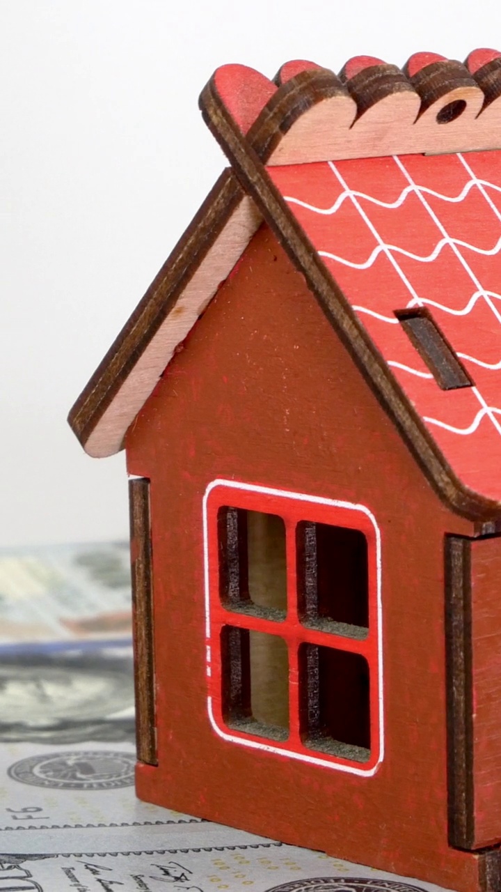 小型家庭住宅的模型站在美元钞票的背景上，缓慢地旋转。