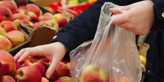 年轻女子的手把苹果放进袋子里。一位顾客正在商店里购物。