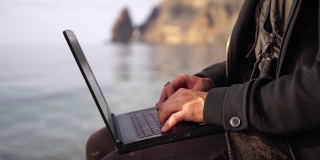 Digital Nomad，一个年轻的纹身男子，在日落时分坐在海滩上，远程在线工作，在笔记本电脑键盘上打字。度假时远程工作，远程经营在线业务