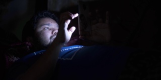 年轻人晚上坐在床上玩智能手机