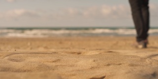 一个男人的剪影走在海边的沙滩上，离开了镜头。平静的海边漫步，模糊的背景，浅景深4K直播视频。蓝天白云，春日艳阳