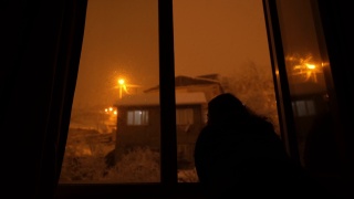 女性剪影从窗口观看雪花飘落的夜晚视频素材模板下载