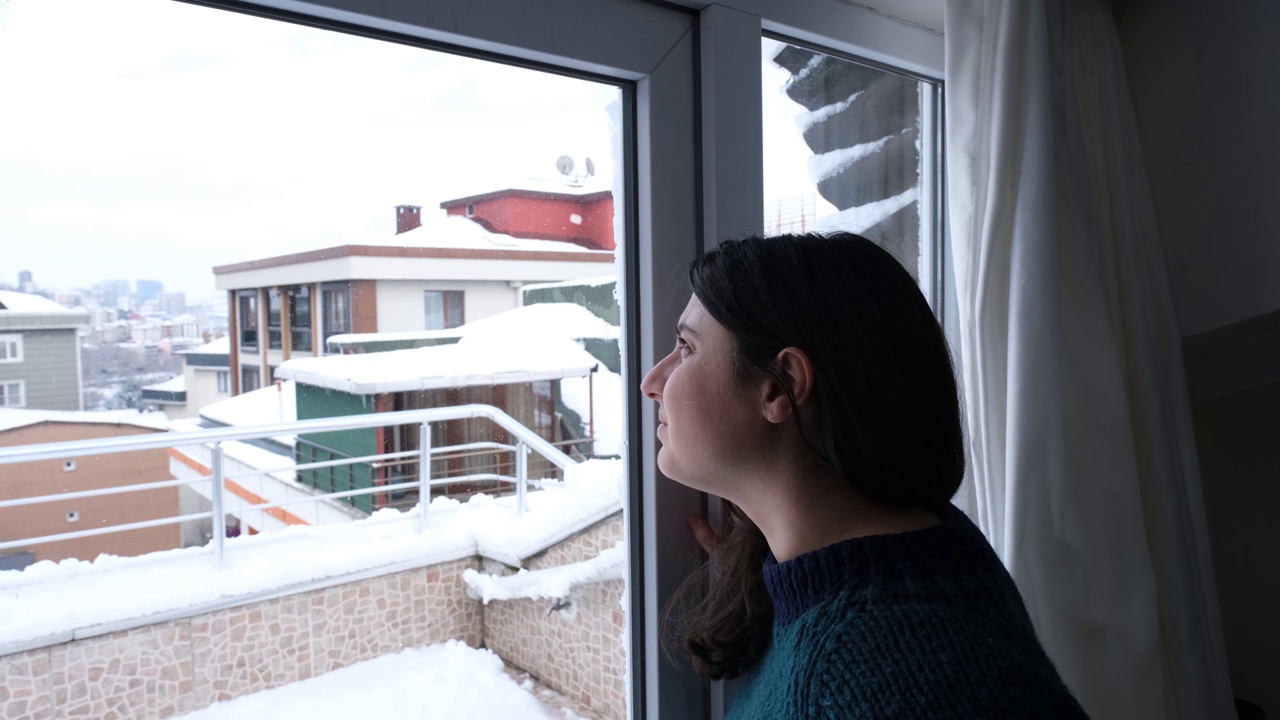 一位女士在冬天看着窗外的雪景