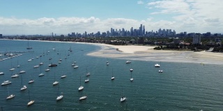 墨尔本城市天际线的美丽景色，从圣基尔达海滩，墨尔本，维多利亚，澳大利亚，在一个阳光明媚但部分多云的日子里，成排的游艇或船只在海洋中。无人机航拍视频。