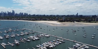 圣基尔达码头位于澳大利亚维多利亚州墨尔本海湾的海滩附近，拥有美丽的CBD或市中心天际线。游艇和帆船停泊在码头上。多云的日子，中午或下午早些时候有太阳。