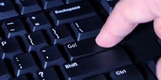男性手指按下计算机键盘上的Go按钮