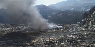 无人机拍摄的大型垃圾填埋场，燃烧的垃圾带着浓重的污染烟雾。