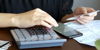 女人在线记账发票对账单与信用卡债务账单，使用计算器计算每月成本，税收，银行账户余额和费用财务在家里