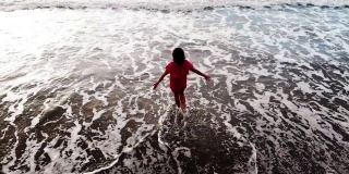 日落时分，身着红色连衣裙的女子走在海边的沙滩上，灵感自由快乐的度假理念，从无人机空中拍摄，从上方观看