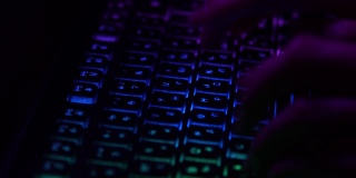 手在彩色键盘上打字非常快。晚上工作。手被紫光照亮。特写镜头