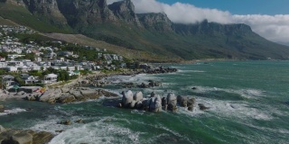 飞上海岸。汹涌的海浪冲击着海岸的岩石。高山峻岭下的住宅区。南非开普敦