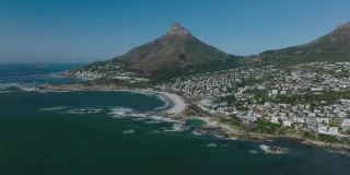 旅游目的地航拍全景画面海滨住宅区，阳光明媚，海滩在海湾。背景是高耸的山峰。南非开普敦