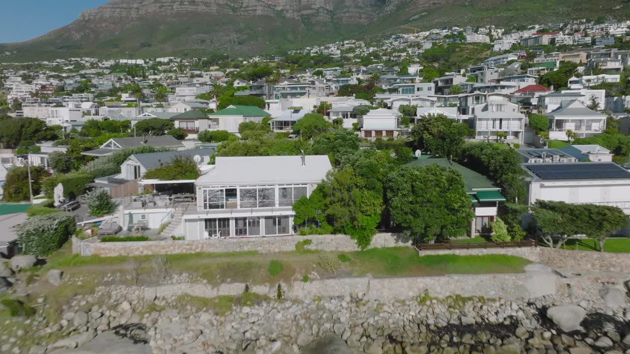 在密集发展的住宅区上面向前飞。阳光明媚的热带旅游目的地的建筑和宾馆。南非开普敦