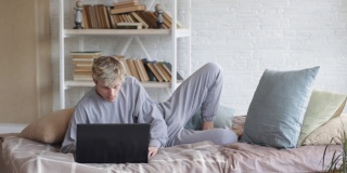 早晨，一个穿着轻睡衣的男人坐在床上，合上笔记本电脑，愉快地跳跃着，享受着生活。